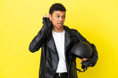 Sarı arka planda izole edilmiş motosiklet kasklı genç Afrikalı Amerikalı bir adam. Kulağına elini sürerek bir şey dinliyor.