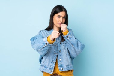 Kafkasyalı genç bir kadın, mavi arka planda yalıtılmış bir şekilde dövüşüyor.