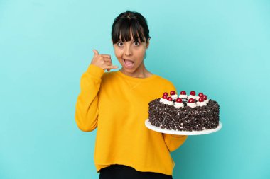 Genç melez bir kadın doğum günü pastası tutuyor ve telefon jesti yapıyor. Bana geri dönüş işareti ver.