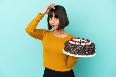 Doğumgünü pastası tutan genç melez kadın yan tarafa bakarken sürpriz jest yapıyor.