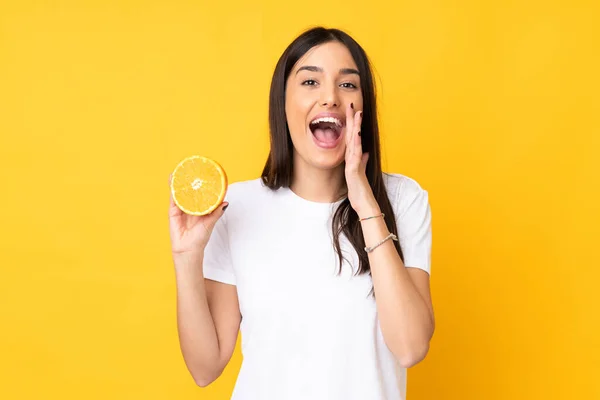 Junge Kaukasische Frau Hält Eine Orange Isoliert Auf Gelbem Hintergrund — Stockfoto