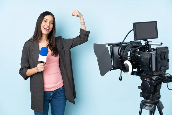 Reporter woman holding a microphone and reporting news isolated on blue background doing strong gesture