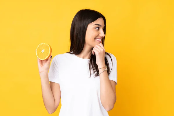 Ung Kaukasiska Kvinna Som Håller Orange Isolerad Gul Bakgrund Tänker — Stockfoto