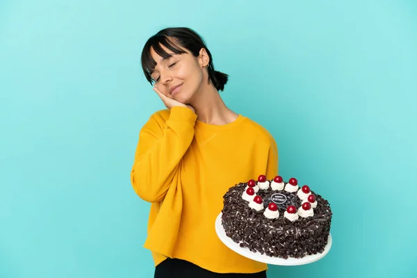 Young mixed race woman holding birthday cake making sleep gesture in dorable expression