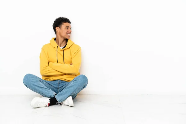 年轻的非洲裔美国人坐在地板上 与白色背景隔离 侧面张望 — 图库照片