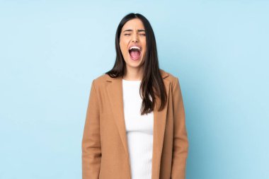 Kafkasyalı genç bir kadın mavi arka planda izole edilmiş ve ağzı açık bağırıyor.