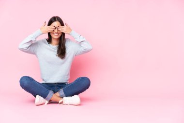 Pembe arka planda izole edilmiş genç beyaz kadın gözlerini elleriyle kapatıyor.