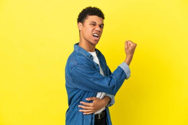 Sarı arka planda izole genç Afrikalı Amerikalı bir adam zaferi kutluyor.