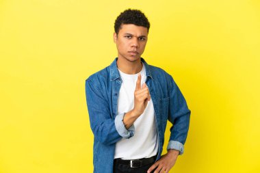 Sarı arka planda izole edilmiş genç Afrikalı Amerikalı hayal kırıklığına uğramış ve ön tarafı işaret ediyor.