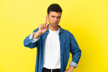 Sarı arka planda izole edilmiş genç Afro-Amerikalı adam ciddi bir ifadeye sahip birini sayıyor.