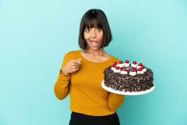 Doğumgünü pastası tutan genç melez kadın şaşırmış ve ön tarafı işaret ediyor.
