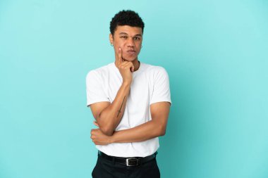Genç Afrikalı Amerikalı adam mavi arka planda izole edilmiş ve düşünüyor