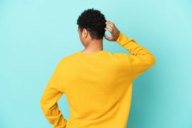 Genç Afrikalı Amerikalı adam mavi arka planda izole edilmiş ve düşünüyor.