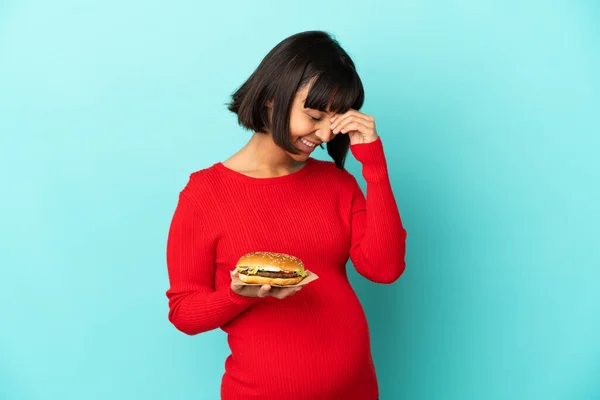 Joven Embarazada Sosteniendo Una Hamburguesa Sobre Fondo Aislado Riendo — Foto de Stock