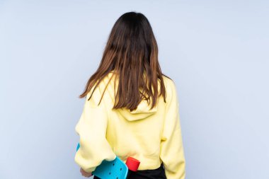 Kafkasyalı genç bir kadın mavi arka planda izole edilmiş ve arka planda kaykay yapıyor.