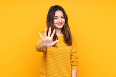 Sarı arka planda izole edilmiş genç beyaz kadın parmaklarıyla beşi sayıyor.