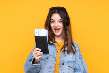 Sarı arka planda izole edilmiş genç beyaz kadın tatilde mutlu pasaport ve uçak biletleriyle