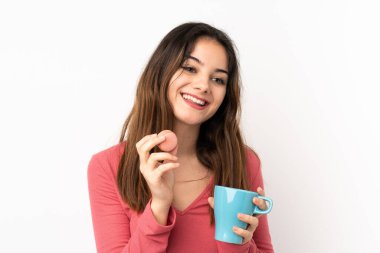 Pembe arka planda soyutlanmış beyaz bir kadın elinde renkli Fransız kurabiyeleri ve bir fincan süt tutuyor.