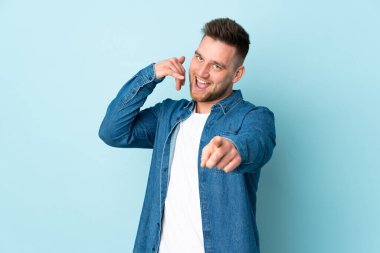 Rus yakışıklı adam mavi arka planda izole edilmiş telefon hareketi yapıyor ve ön tarafı işaret ediyor.