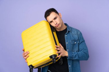 Beyaz tenli yakışıklı, mor arka planda izole edilmiş seyahat valiziyle ve mutsuz.