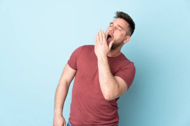 Rus yakışıklı adam izole edilmiş arka planda esniyor ve ağzını eliyle açık tutuyor.