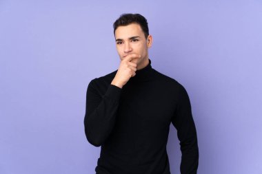 Balıkçı yaka kazaklı, mor arka planda izole edilmiş, kuşkulu ve kafası karışık genç beyaz bir adam.