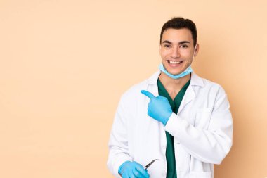 Genç dişçi bej arka planda izole araçlar tutuyor. Şaşırmış ve işaret ediyor.