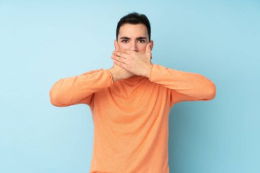 Beyaz tenli yakışıklı adam mavi arka planda izole edilmiş, ağzı elleriyle kapatıyor.