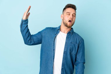 Rus yakışıklı adam mavi arka planda izole edilmiş, yorgun ve hasta yüzlü.