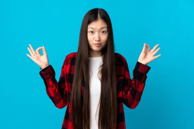 Zen pozisyonunda, izole edilmiş mavi arka planı olan genç bir Çinli kız.