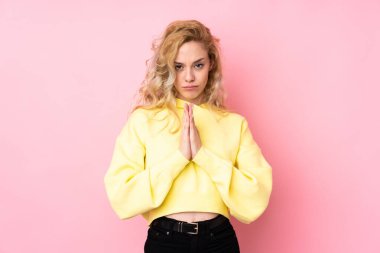 Pembe arka planda izole edilmiş sweatshirt giyen genç sarışın kadın avuç içlerini bir arada tutuyor. İnsan bir şey ister.