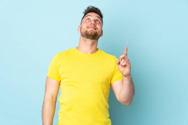 Rus yakışıklı adam mavi arka planda izole edilmiş yukarı bakıyor ve şaşırıyor.