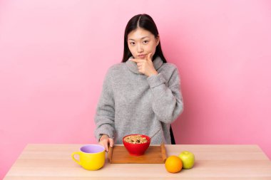 Genç Çinli kız kahvaltısını bir masada yapıyor.