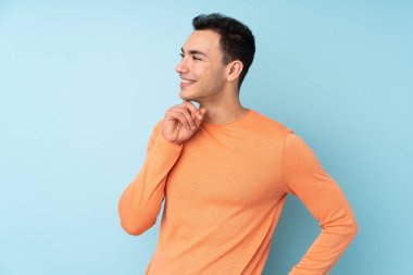 Kafkasyalı yakışıklı genç adam mavi arka planda izole edilmiş bir şekilde yukarı bakarken bir fikir düşünüyor.