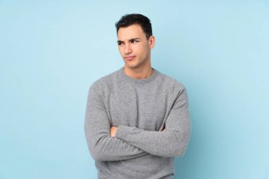 Kafkasyalı yakışıklı genç bir adam mavi arka planda izole edilmiş bir fikir düşünüyor.