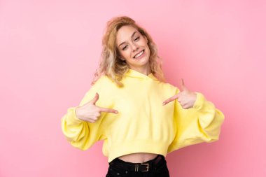 Pembe arka planda izole edilmiş sweatshirt giyen genç sarışın kadın gururlu ve kendini beğenmiş.