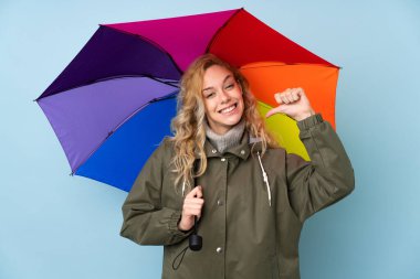 Mavi arka planda şemsiyesi olan genç sarışın kadın gururlu ve kendini beğenmiş.