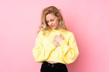 Pembe arka planda izole edilmiş kazak giyen genç sarışın bir kadın. Kalbinde ağrı var.