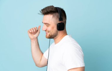 Rus yakışıklı adam mavi arka planda izole edilmiş müzik ve dans dinliyor.