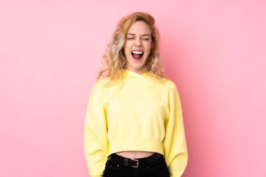 Pembe arka planda izole edilmiş bir sweatshirt giyen genç sarışın kadın ağzı açık bir şekilde öne doğru bağırıyor.
