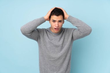 Mavi arka planda yalıtılmış beyaz, yakışıklı, şaşırtıcı bir yüz ifadesi olan genç adam.