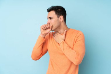 Mavi arka planda yaşayan beyaz tenli yakışıklı adam öksürük ve kötü hissetmekten muzdarip.