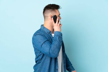 Rus yakışıklı adam mavi arka planda izole edilmiş cep telefonuyla biriyle sohbet ediyor.