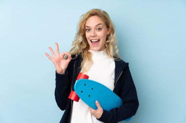 Genç sarışın kadın mavi arka planda izole edilmiş ve paten kayıyor.