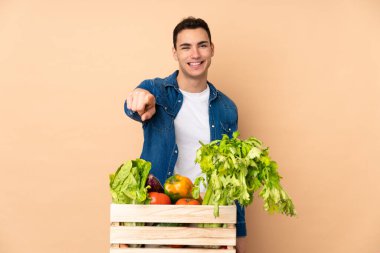 Bej arka planda izole edilmiş bir kutuda taze sebze toplayan çiftçi kendine güvenen bir ifadeyle sana parmak kaldırıyor.