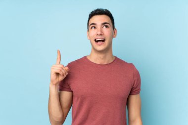Genç, beyaz, yakışıklı bir adam mavi arka planda izole edilmiş. Çözümü bulmak için parmağını kaldırıyor.