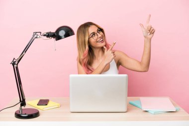 İşyerinde pembe arka planda dizüstü bilgisayarı olan genç bir bayan öğrenci işaret parmağıyla işaret etmek harika bir fikir.