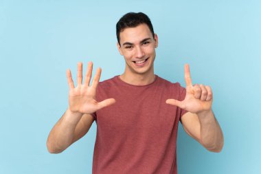 Mavi arka planda izole edilmiş beyaz tenli yakışıklı adam yediyi parmaklarıyla sayıyor.