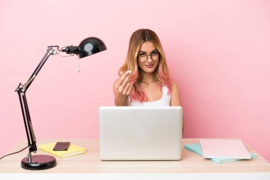 Pembe arka planda dizüstü bilgisayarı olan genç bir bayan iş yerinde para hareketi yapıyor.