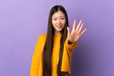 İzole edilmiş mor arka planı olan genç Çinli kız parmaklarıyla beşi sayıyor.